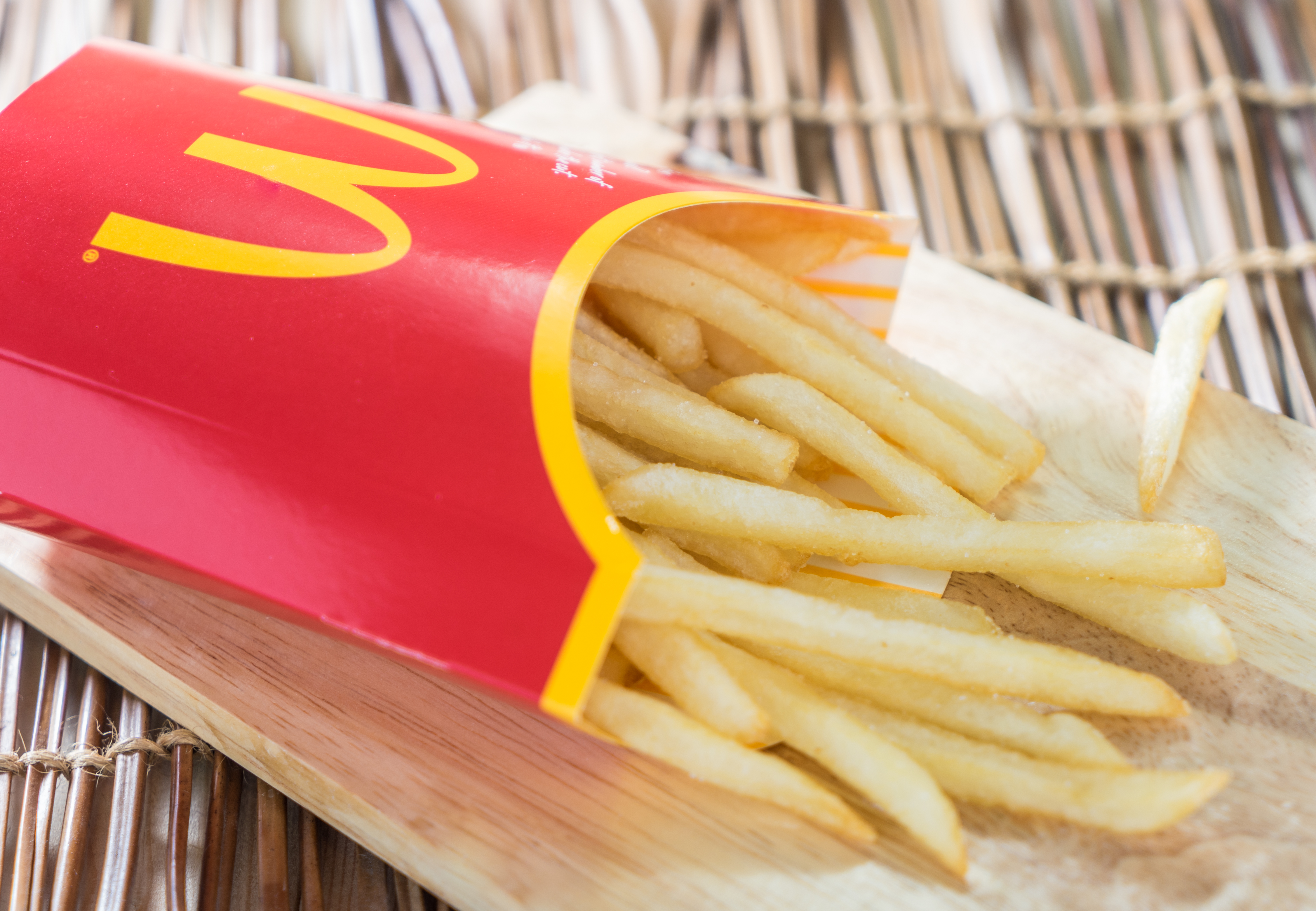 A box of Mc Donalds French Fries on a wooden tray.