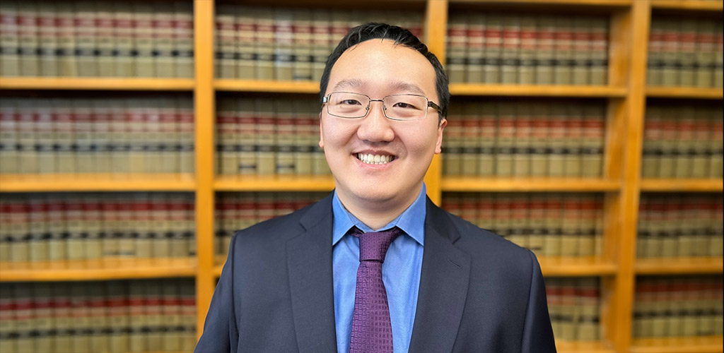Henry Zhu standing in front of a bookcase filled with legal books