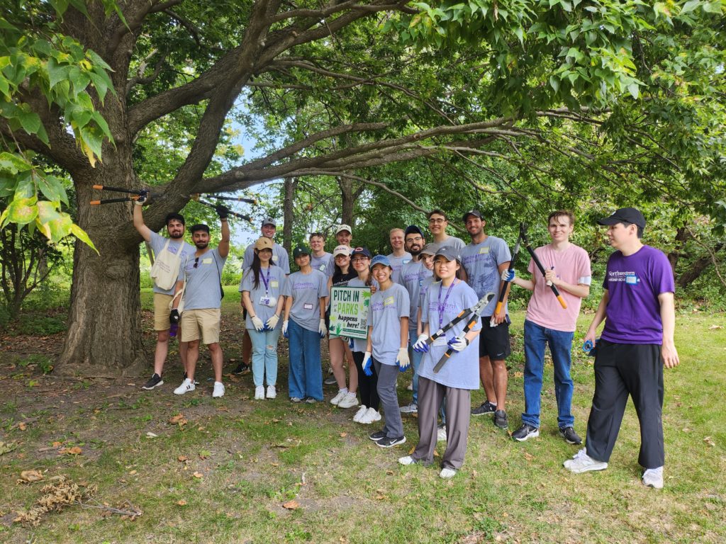 Several students posing in a park with branch clippers and a sign that says "PITCH IN PARKS"