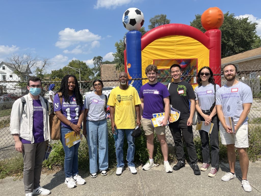 Eight individuals standing in front of a chainlink fence and bounce house. 