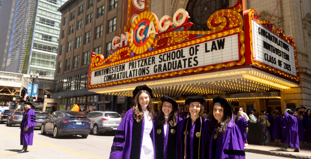 Four women in purple Northwestern regalia stand under the Chicago Theatre marquee honoring Northwestern Pritzker School of Law graduates