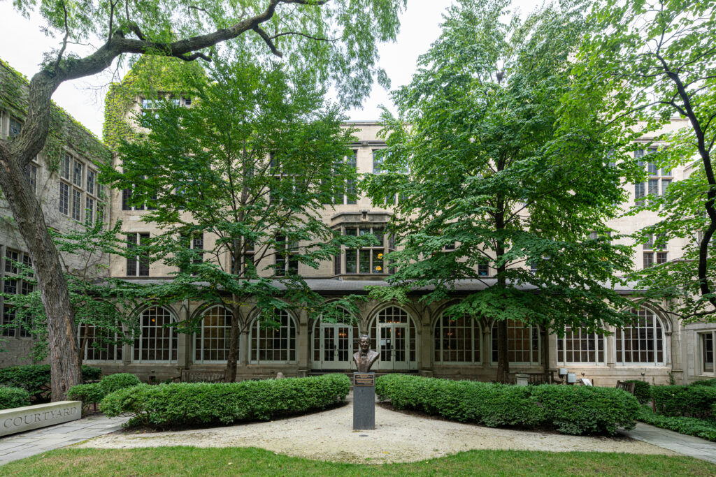 Image of the Justice John Paul Stevens Courtyard at Northwestern Pritzker Law. A bust of Justice Stevens is flanked on each side by shrubs and trees. 
